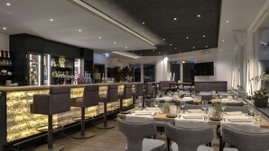 A modern restaurant with a bar area, high chairs, and neatly arranged tables with place settings. - Höll am Main (Ruesselsheim)