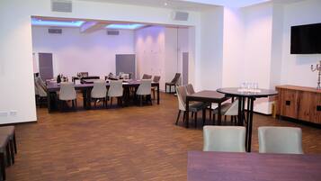 A modern dining area with multiple tables and chairs, a flat-screen TV mounted on the wall, and a wooden cabinet.