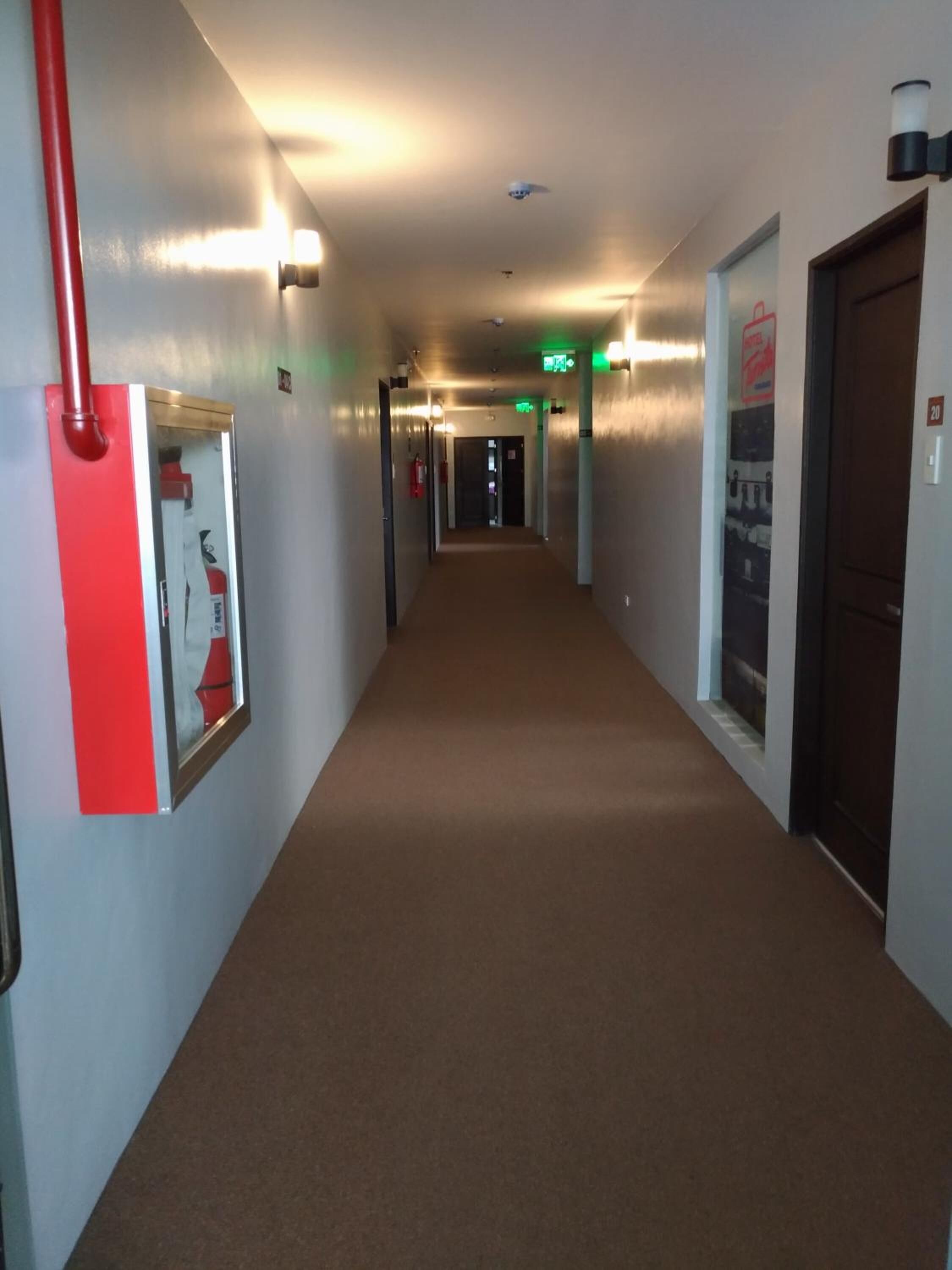 Un pasillo de hotel con piso alfombrado, paredes con luminarias y puertas indicadas con números de habitación.
