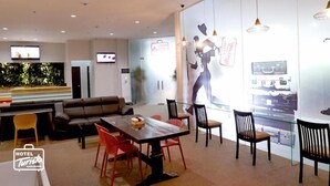 A modern hotel lobby with a dining area, a sofa, and a TV screen. - Hotel Turista Canlubang (Calamba)