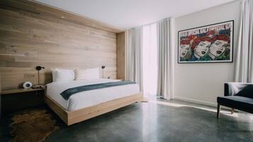 A modern bedroom with a wooden headboard, a large bed, a black bench, and a poster on the wall.