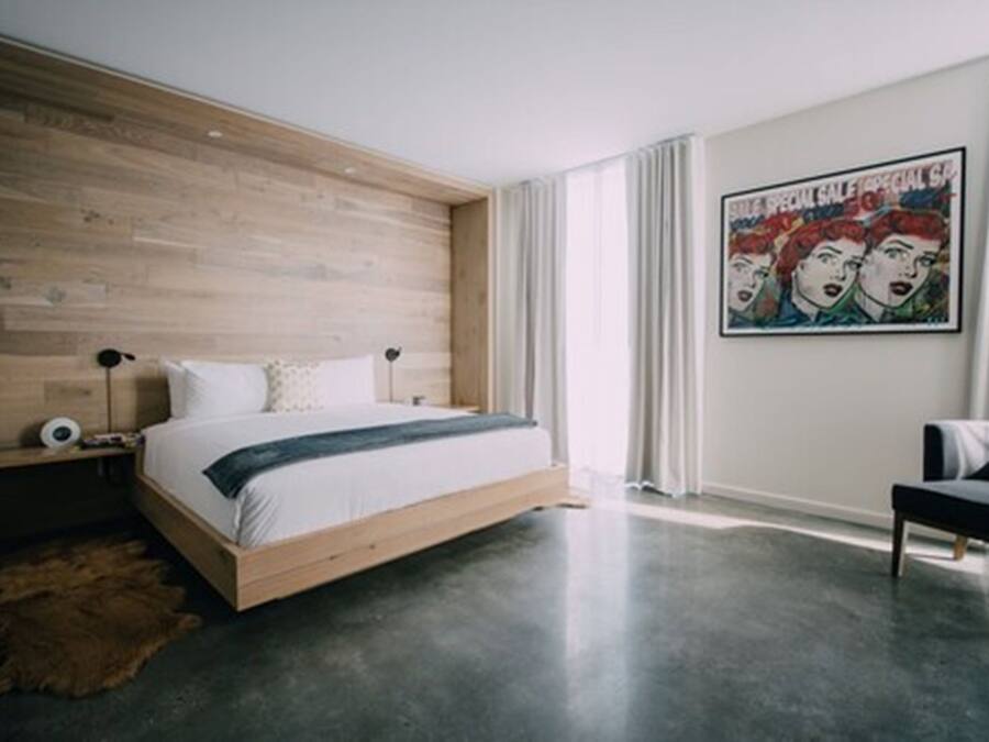 A modern bedroom with a wooden headboard, a large bed, a black bench, and a poster on the wall.