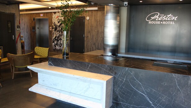 Een receptiegedeelte met een marmeren balie, houten wanden en een groot verticaal bord voor The Preston House & Hotel.