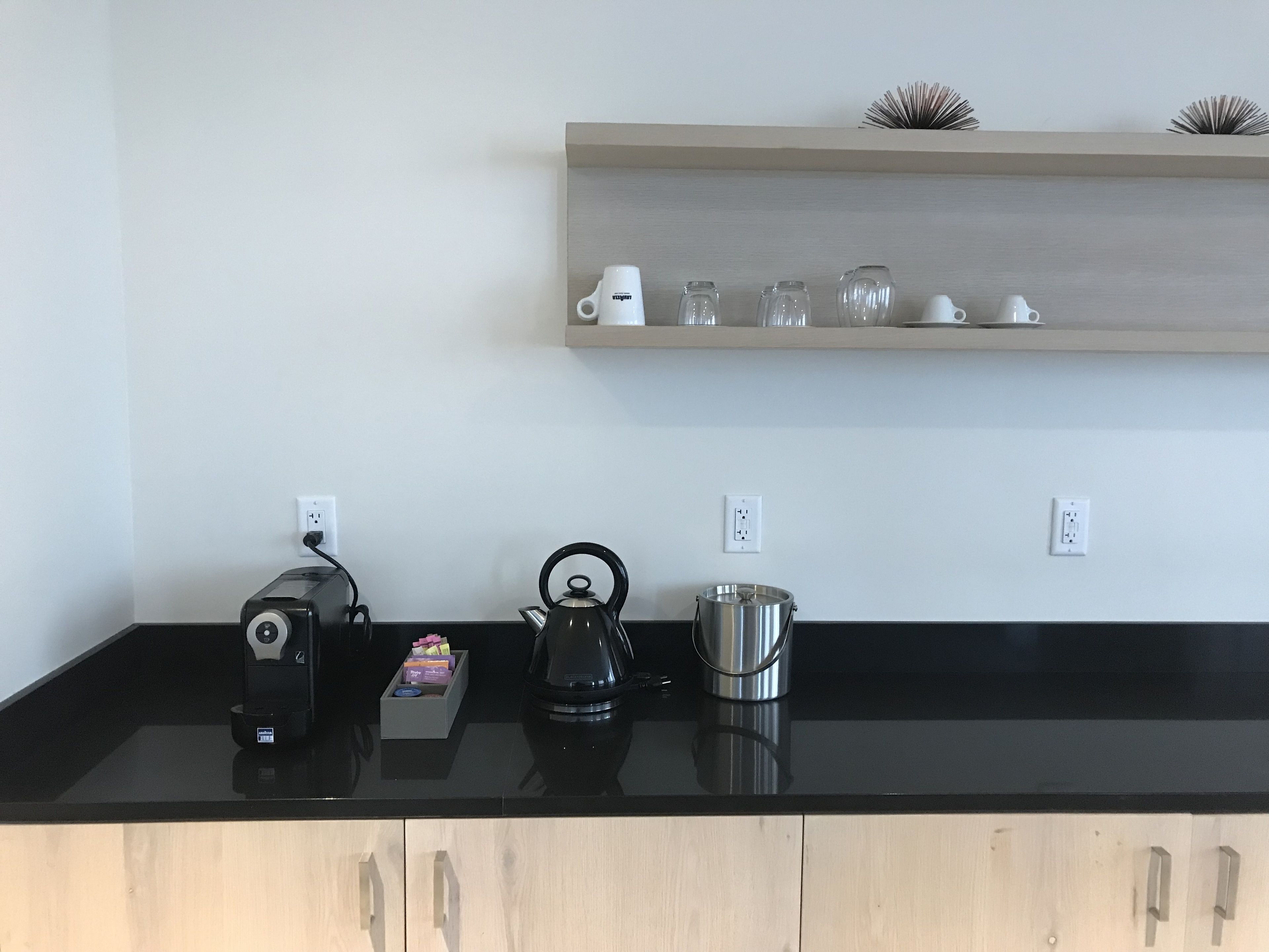 Una encimera de cocina con cafetera, hervidor y olla. Hay tres enchufes en la pared sobre la encimera.