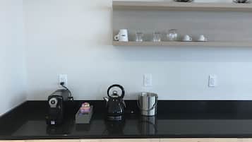 Una encimera de cocina con cafetera, hervidor y olla. Hay tres enchufes en la pared sobre la encimera.