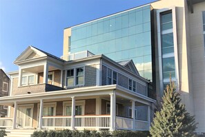 A two-story house with a balcony and a modern building in the background. - The Preston House & Hotel (Riverhead)