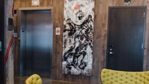Een hal met geel gestoffeerde stoelen, een ronde houten tafel en een groot abstract schilderij aan de muur.