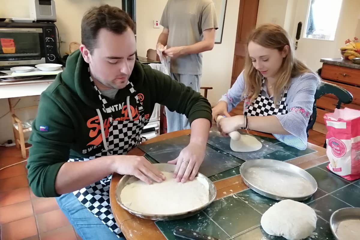 A kitchen with a microwave, a checkered apron, and a woman rolling dough on a table.