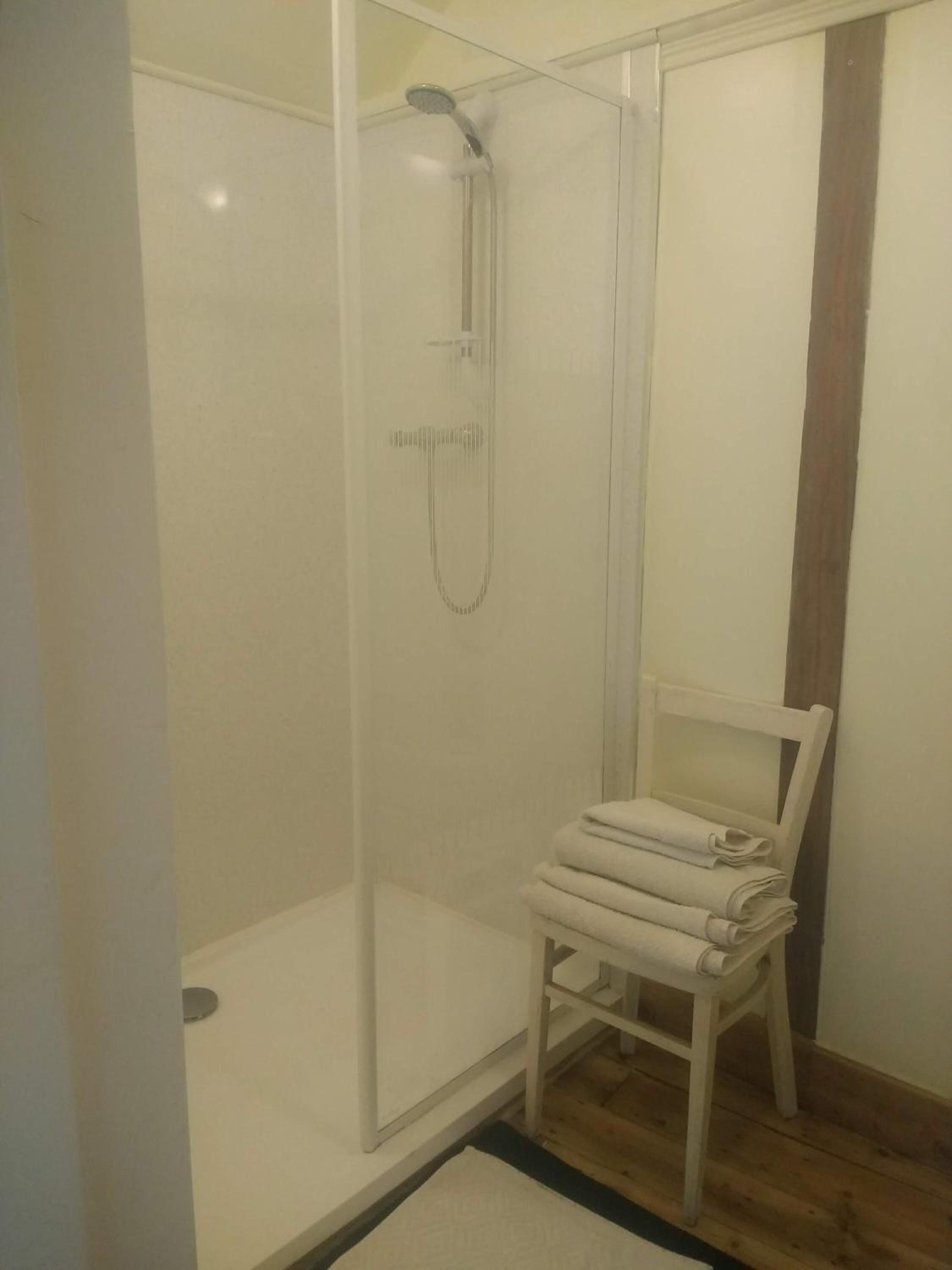 A shower enclosure with a glass door, a white towel chair, and a wooden floor.