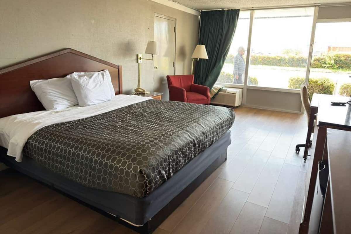Ein Hotelzimmer mit einem großen Bett, einem Schreibtisch, einem Stuhl und einem Vorhangfenster.