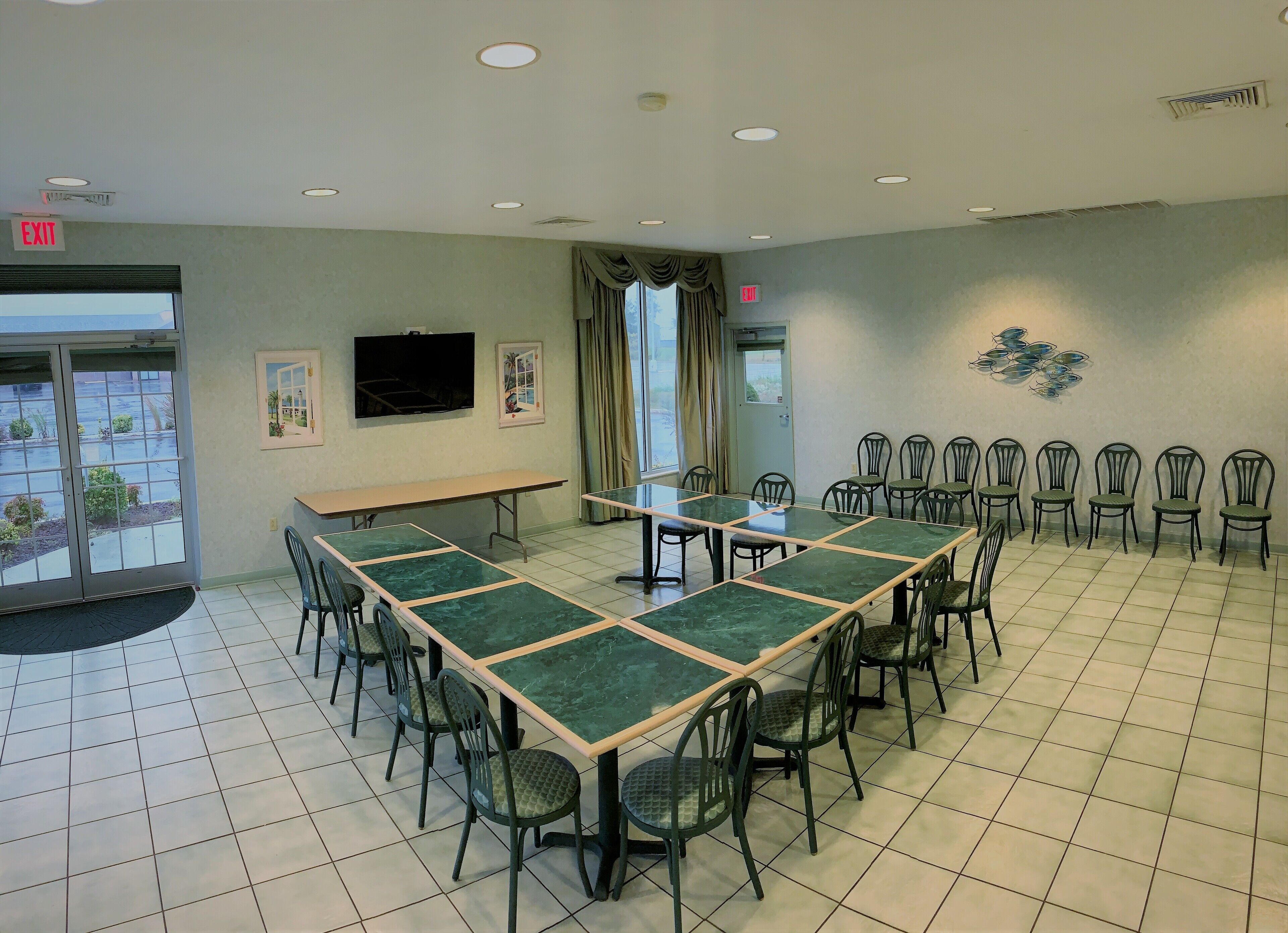 A conference room with a long table, chairs, a TV, and exit signs.