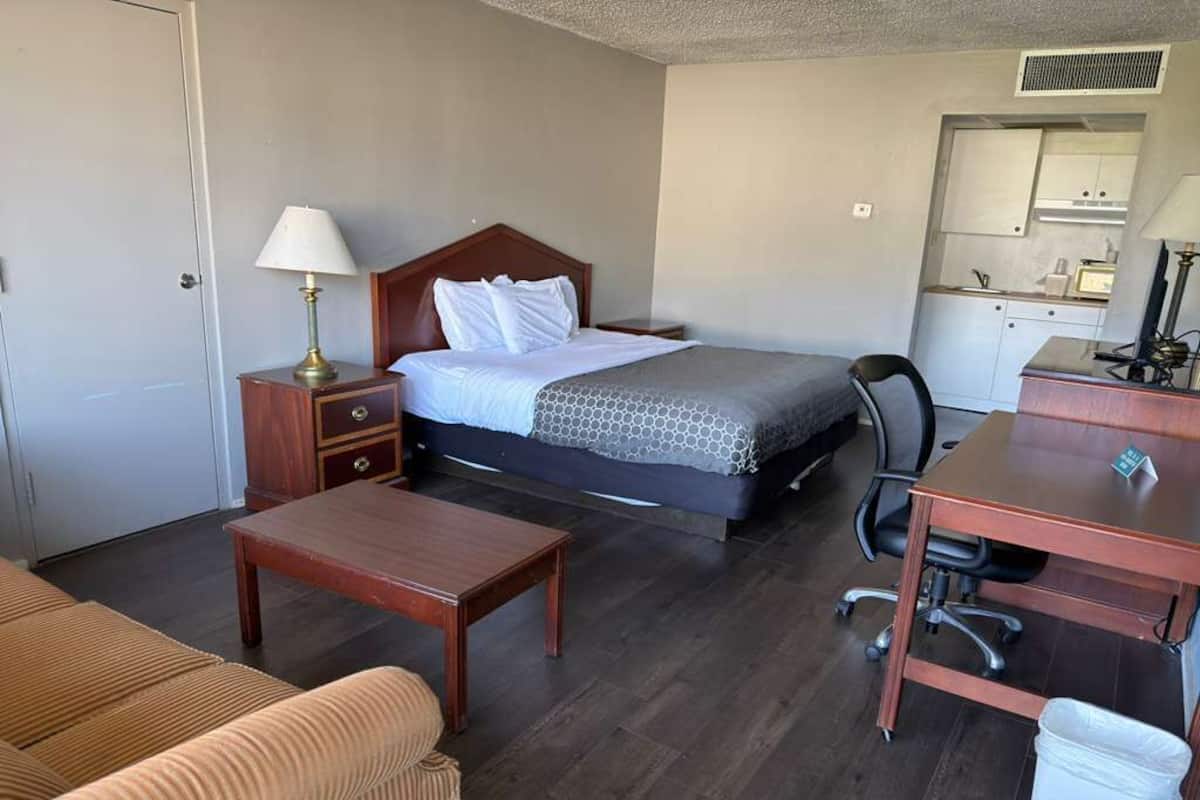 Ein Hotelzimmer mit Bett, Nachttisch, Lampe, Schreibtisch, Stuhl und einer kleinen Küchenzeile.