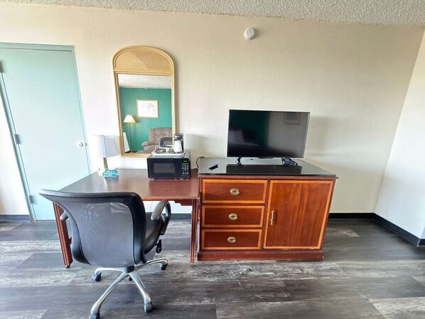Una habitación de hotel con un escritorio de madera, un televisor, una silla, un espejo y una puerta.