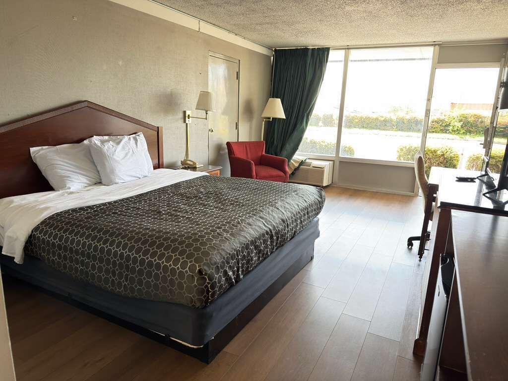 Een hotelkamer met een groot bed, een bureau, een stoel, een raam met gordijnen en een lamp.