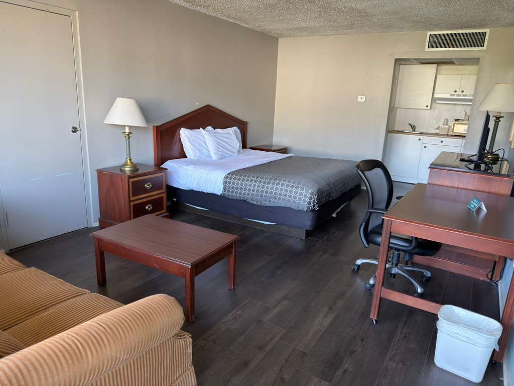 A hotel room with a bed, a desk, a chair, a small table, a sofa, a kitchenette, and a bathroom.