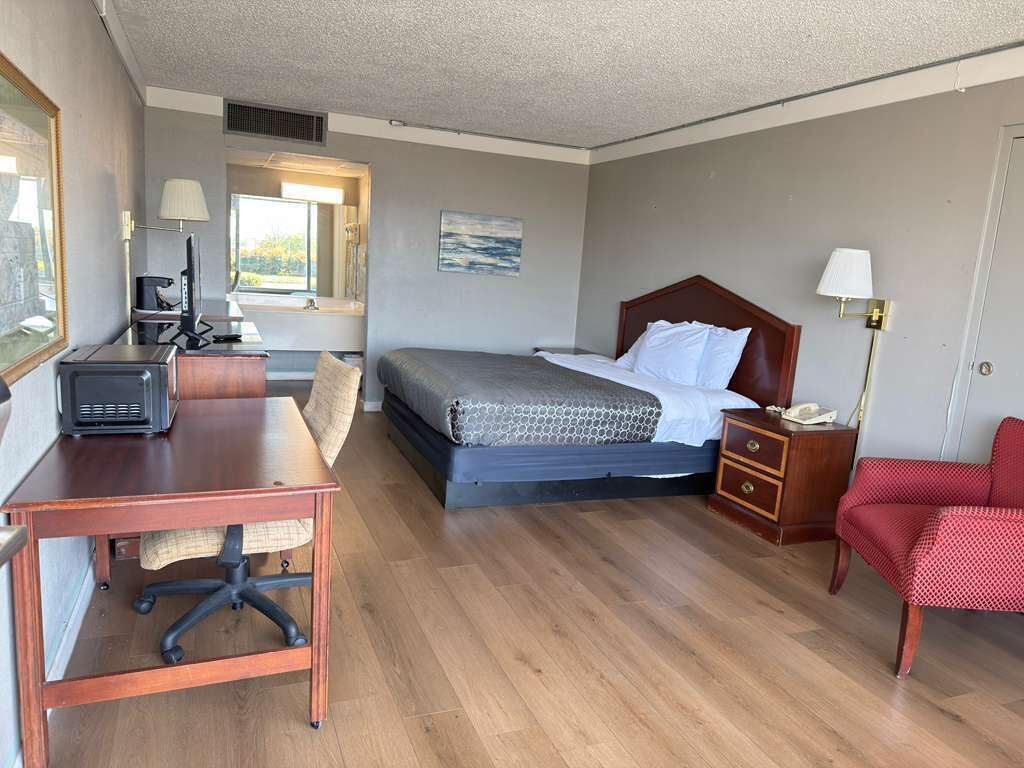 Une chambre d’hôtel avec un lit, un bureau, une chaise et une petite table avec une lampe.