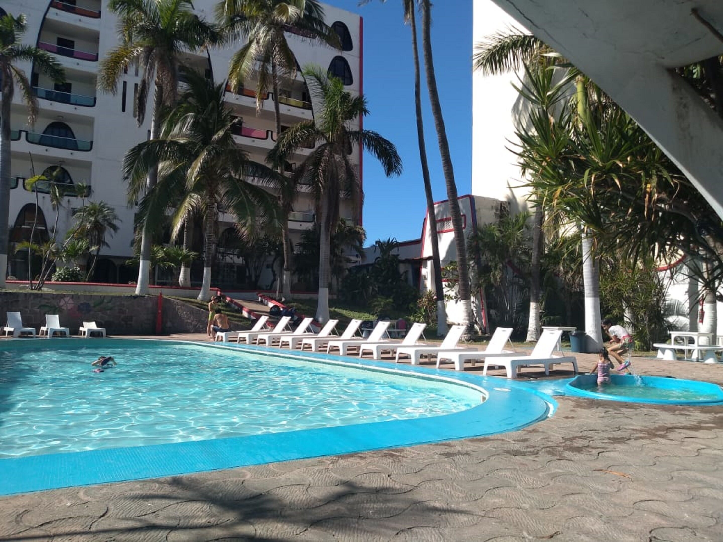 A pool area with lounge chairs and palm trees, surrounded by a building with balconies.