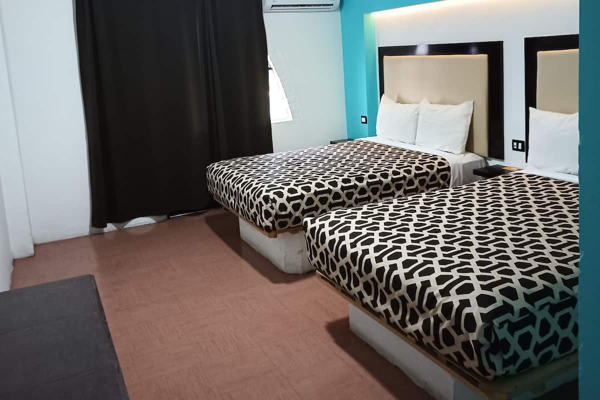A hotel room with two beds, a window with black curtains, an air conditioning unit, and a ceiling light.