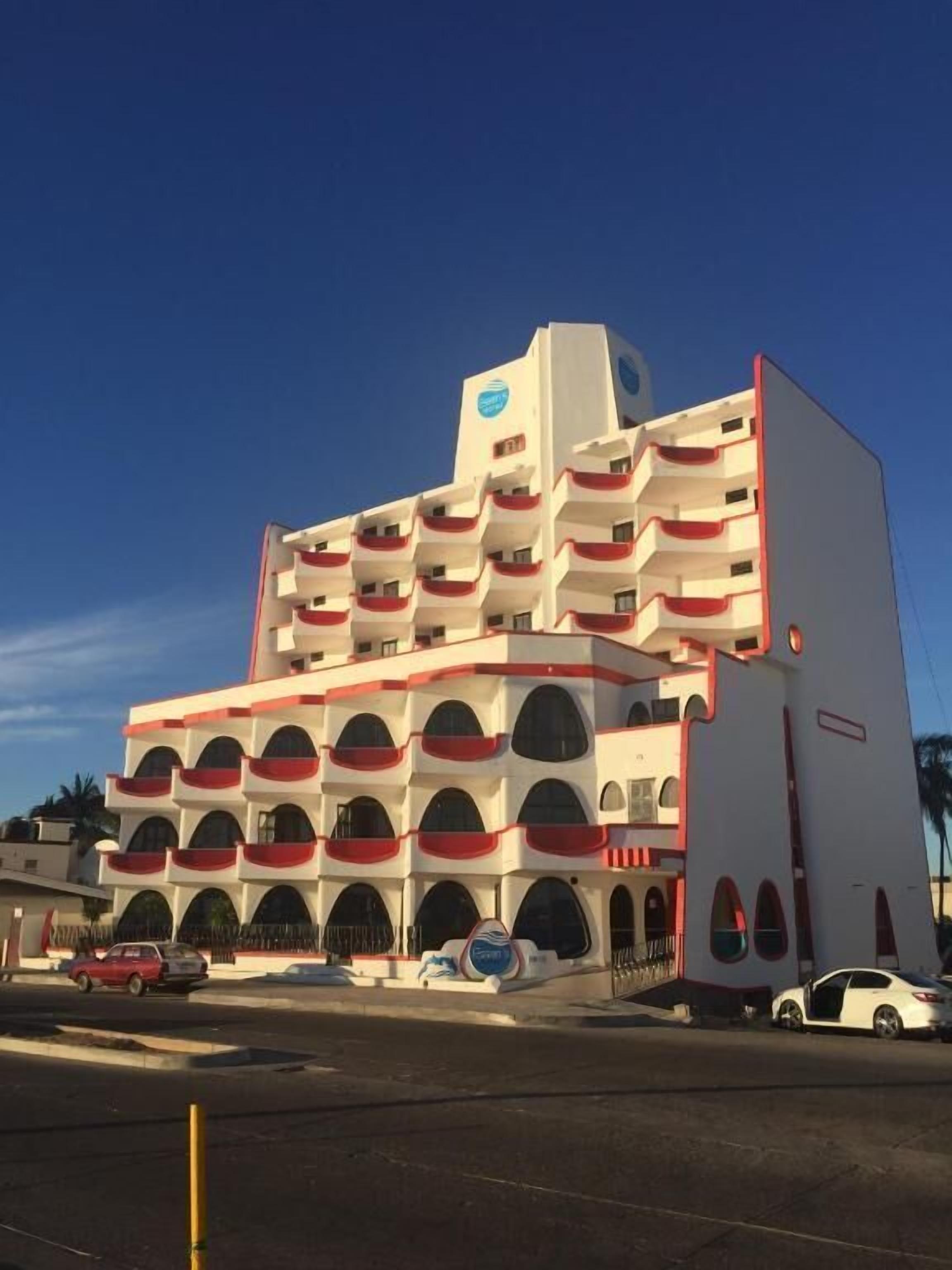A multi-story hotel with a distinctive architectural design featuring balconies and a prominent logo on the top.
