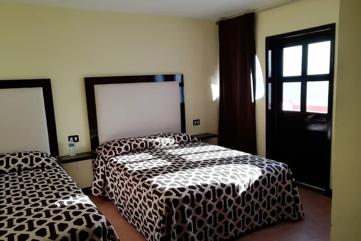 A hotel room with two beds, a window with curtains, and a door.