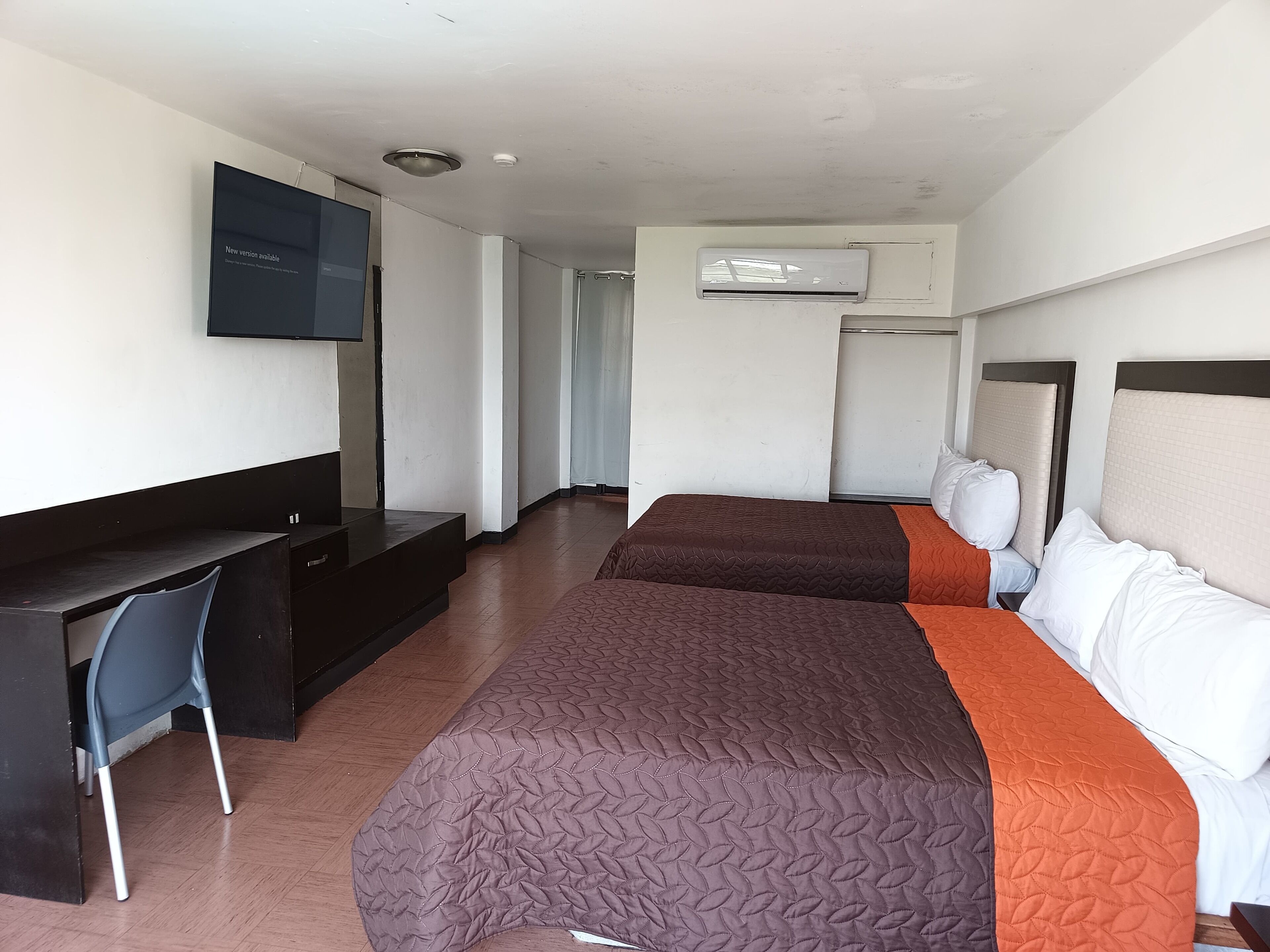 A hotel room with two beds, a desk, a chair, a TV, and an air conditioning unit.