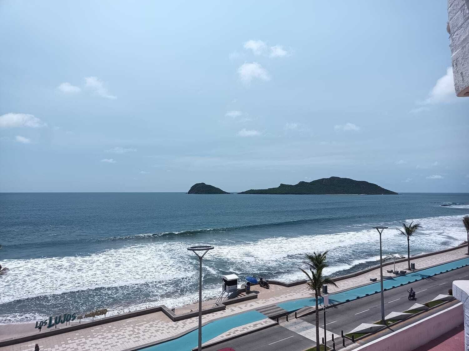 Vista costera con un paseo pavimentado, una piscina y una carretera con vehículos.
