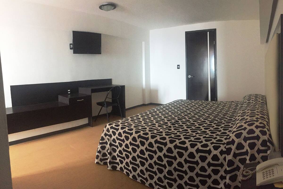 A room with a bed, a desk, a chair, a TV, and a phone.