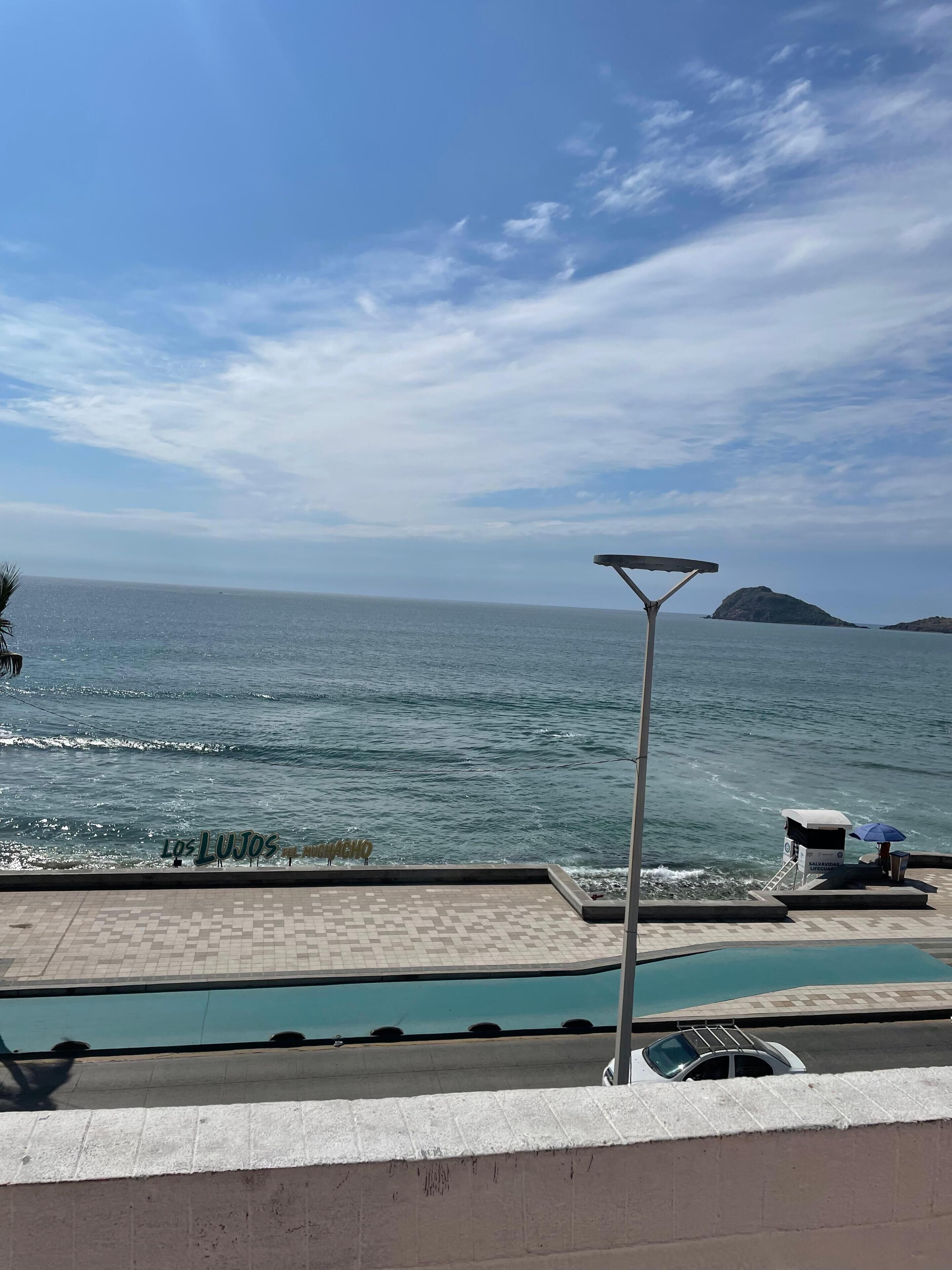 Zona de piscina con vista al mar, puesto de salvavidas y un letrero que dice "Los Lujos".