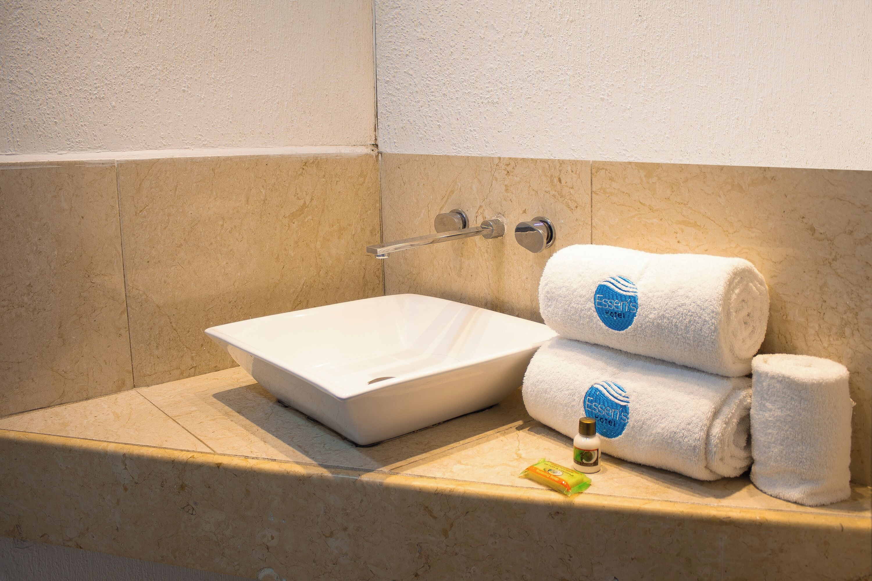 A bathroom with a white sink, two rolled towels, and a small bottle of lotion.