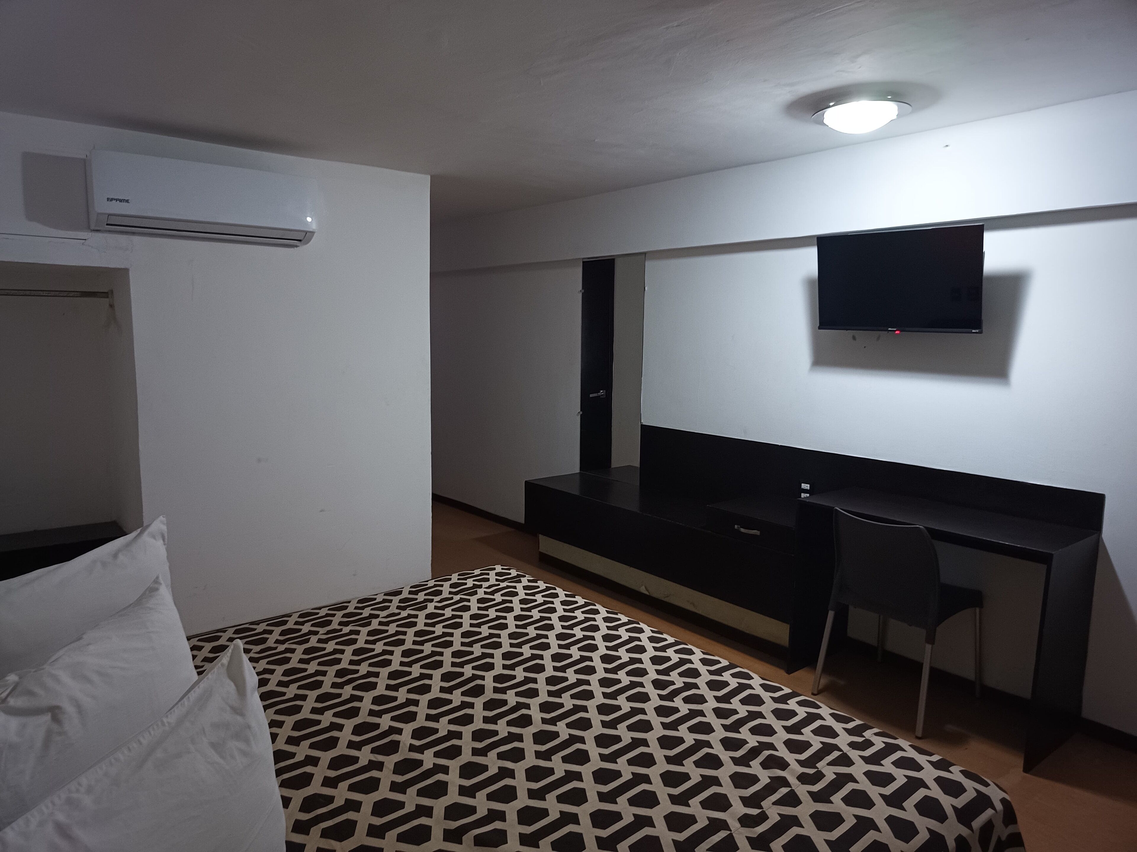 A hotel room with a bed, a desk, a chair, a TV, and an air conditioning unit.
