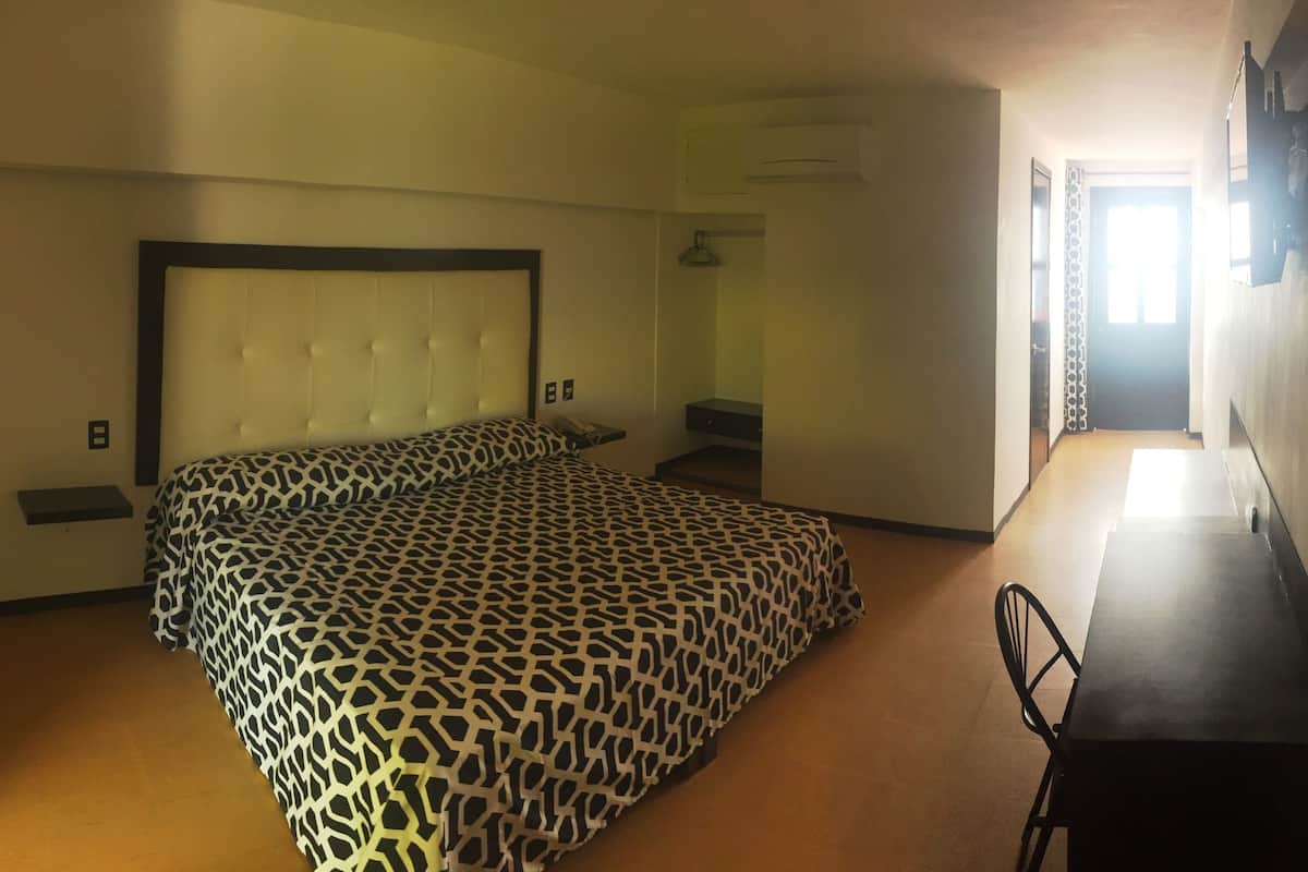 A hotel room with a bed, bedside table, chair, and a desk with a chair.