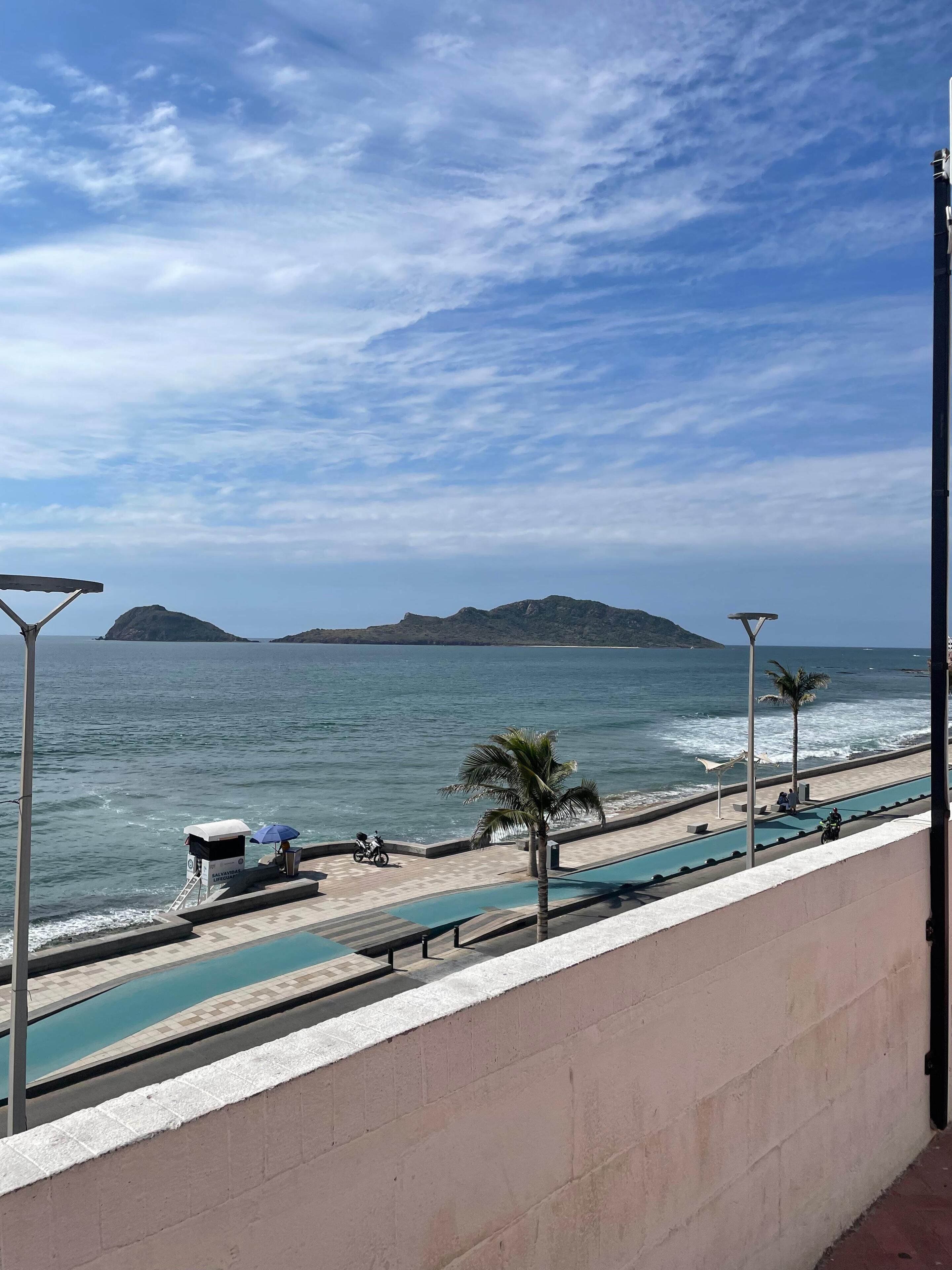 A poolside view with a clear sky, a beach, and distant islands.