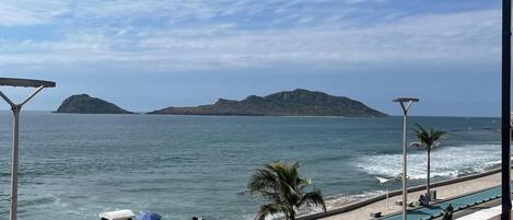A poolside view with a clear sky, a beach, and distant islands.