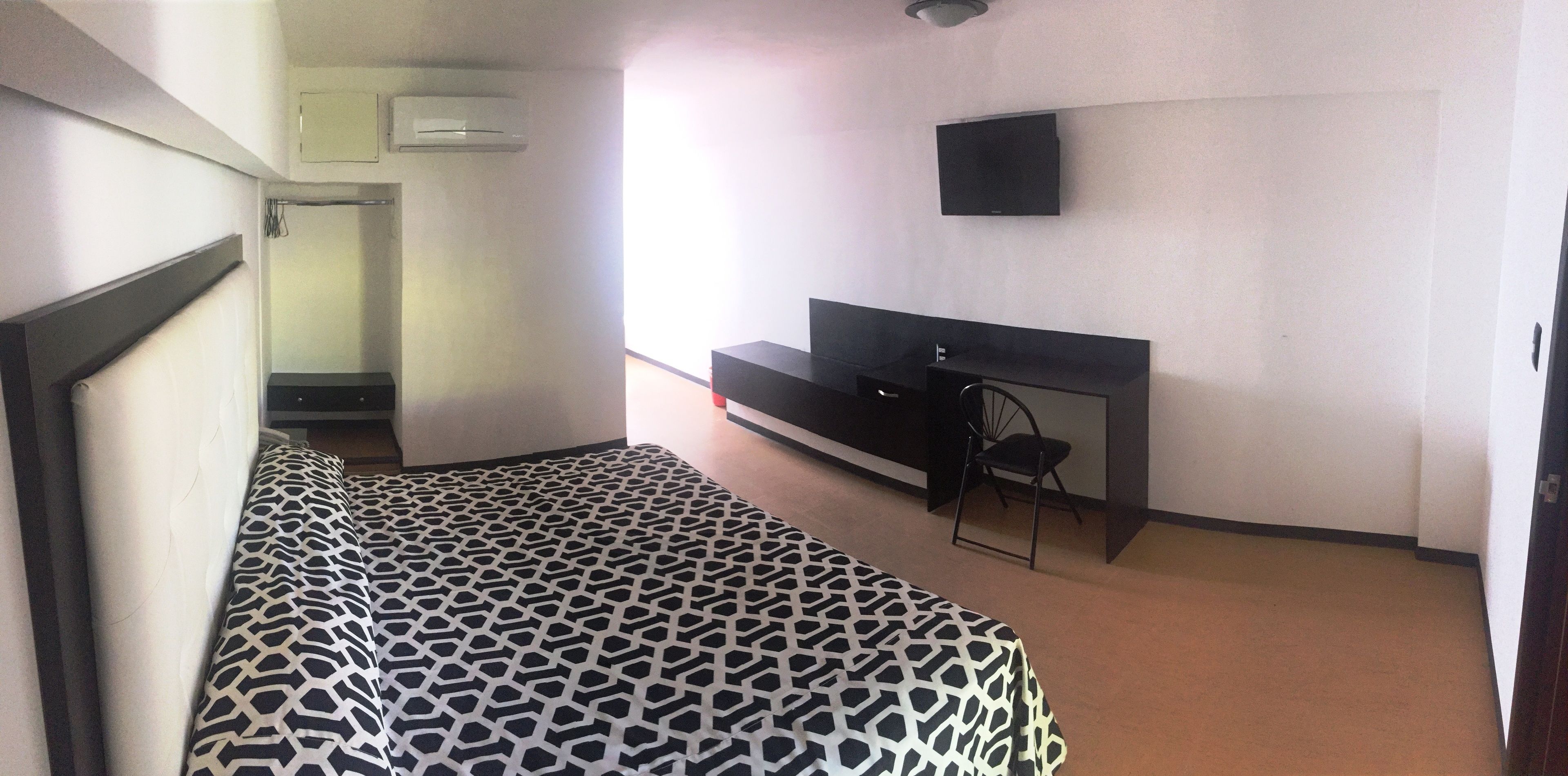 A bedroom with a bed, a TV mounted on the wall, and a desk with a chair.