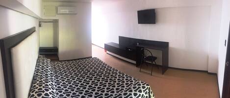 A bedroom with a bed, a TV mounted on the wall, and a desk with a chair.