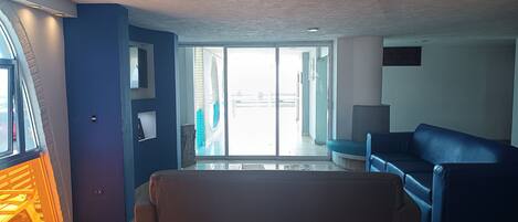 Un salón amplio con un sofá azul, un ventanal grande y puertas corredizas de vidrio que dan a un balcón exterior.