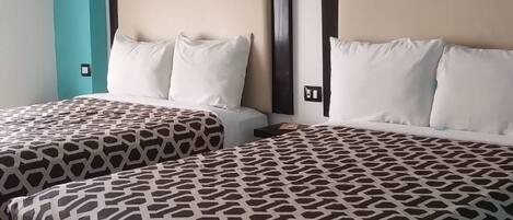 Habitación de hotel con dos camas, cada una con una colcha estampada y almohadas blancas. Las paredes son color verde azulado y el cabecero es de madera.
