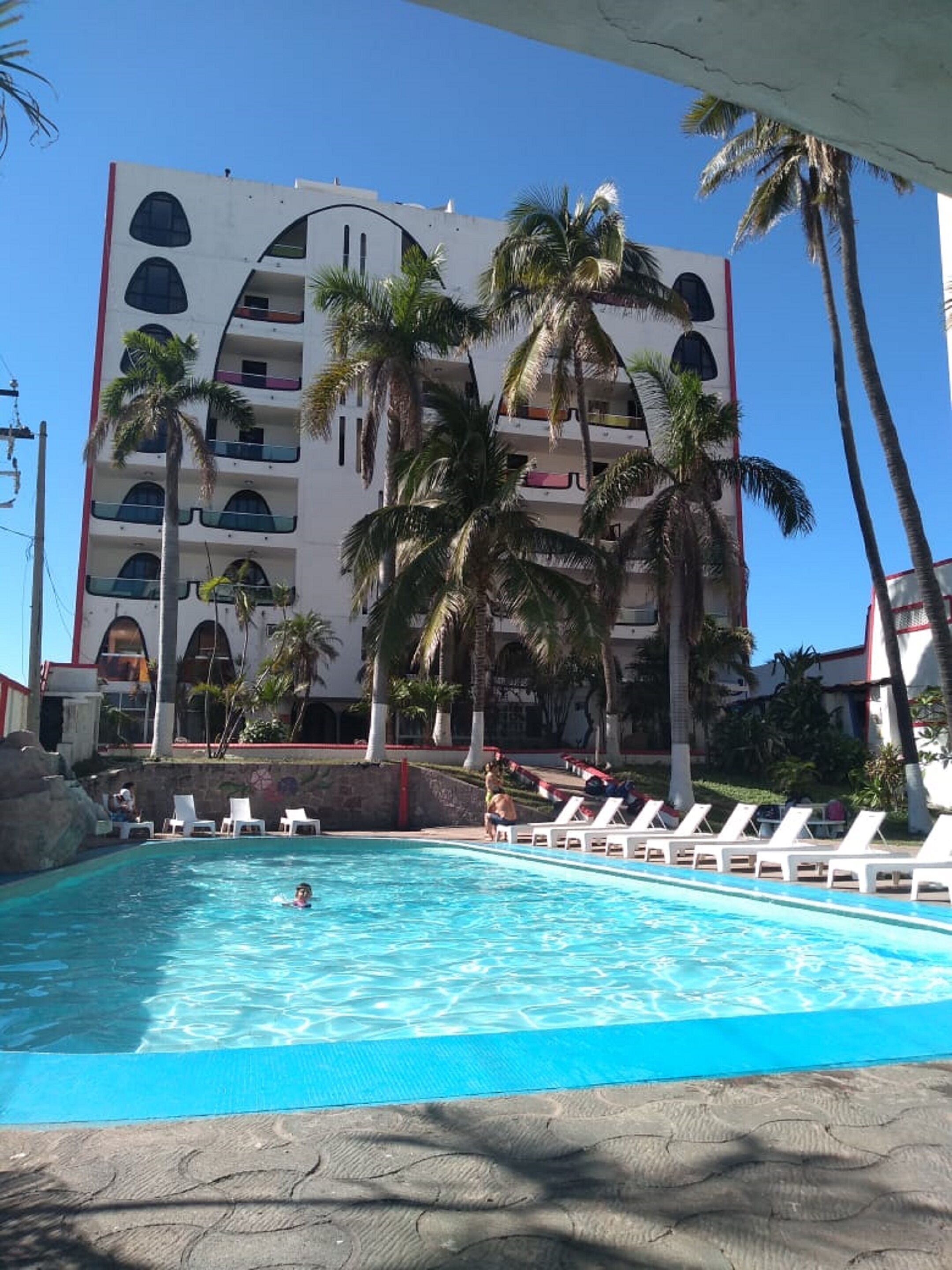 A hotel with a swimming pool, palm trees, and a multi-story building with balconies.
