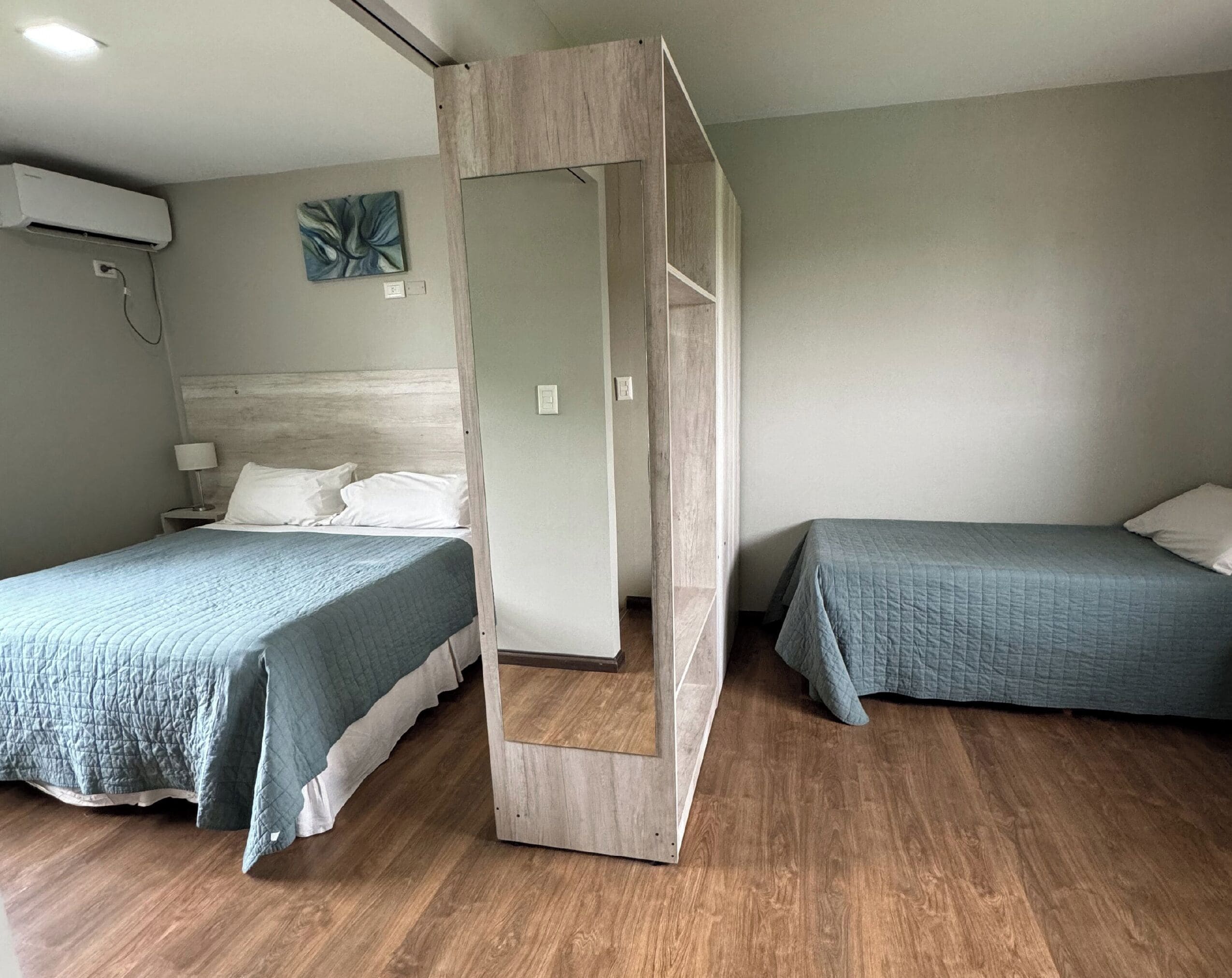 Une chambre d’hôtel avec deux lits, un plancher en bois, un climatiseur fixé au mur et un tableau.