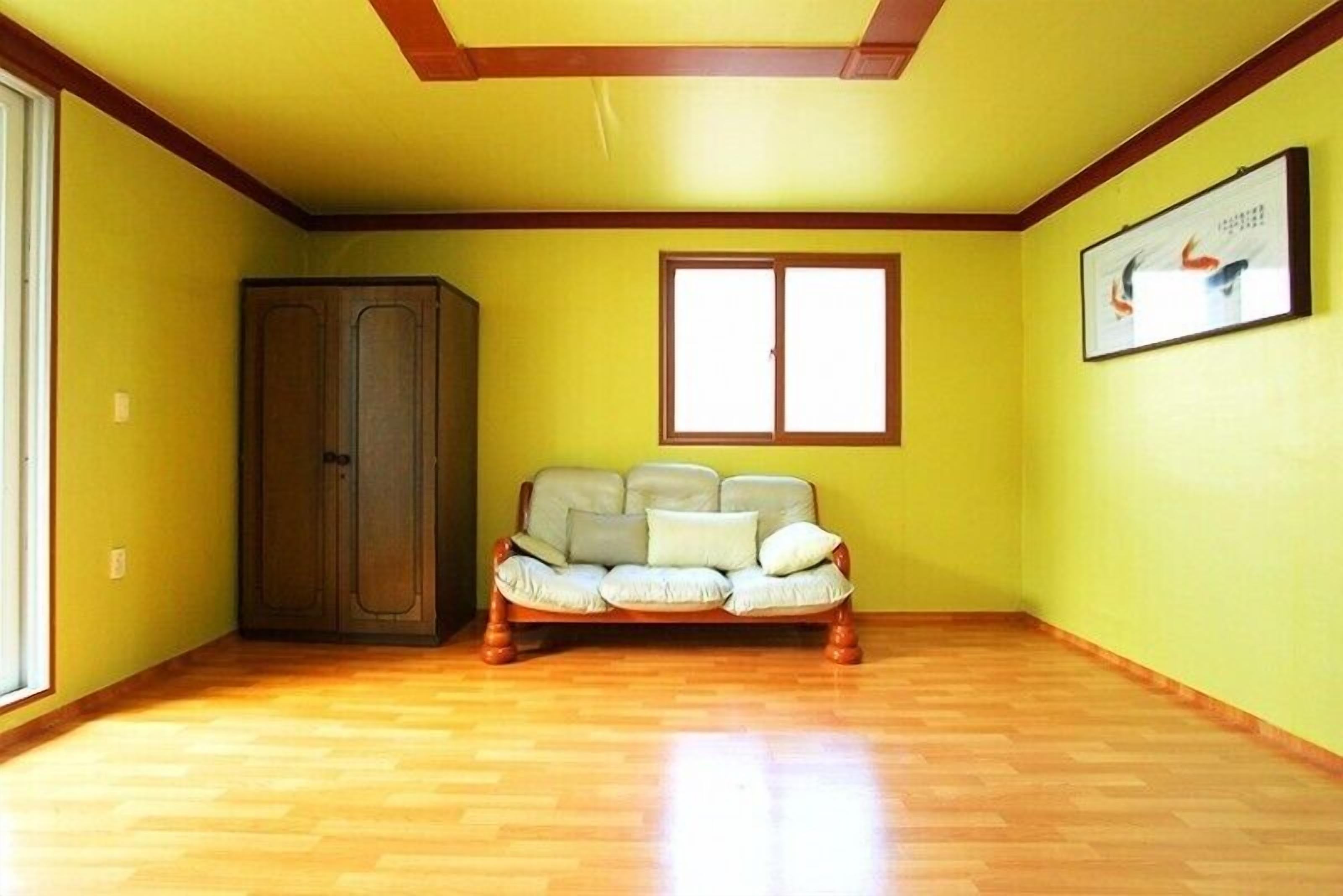 A room with a wooden floor, a sofa, a wardrobe, and a window with a picture on the wall.