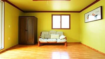 A room with a wooden floor, a sofa, a wardrobe, and a window with a picture on the wall.