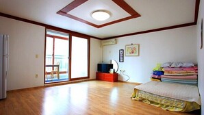 A spacious room with wooden flooring, a bed with colorful bedding, a small TV, and a sliding glass door leading to a balcony. - Yeongheungdo Seayard Pension (Incheon)