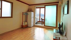 A spacious room with wooden flooring, a large sliding glass door leading to a balcony, a white refrigerator, and a small table with a chair. - Yeongheungdo Seayard Pension (Incheon)