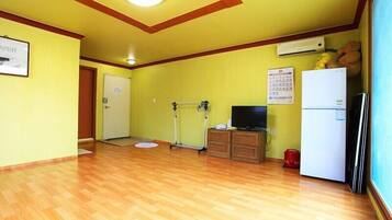 A room with wooden flooring, a television, a refrigerator, and a door leading to another room.