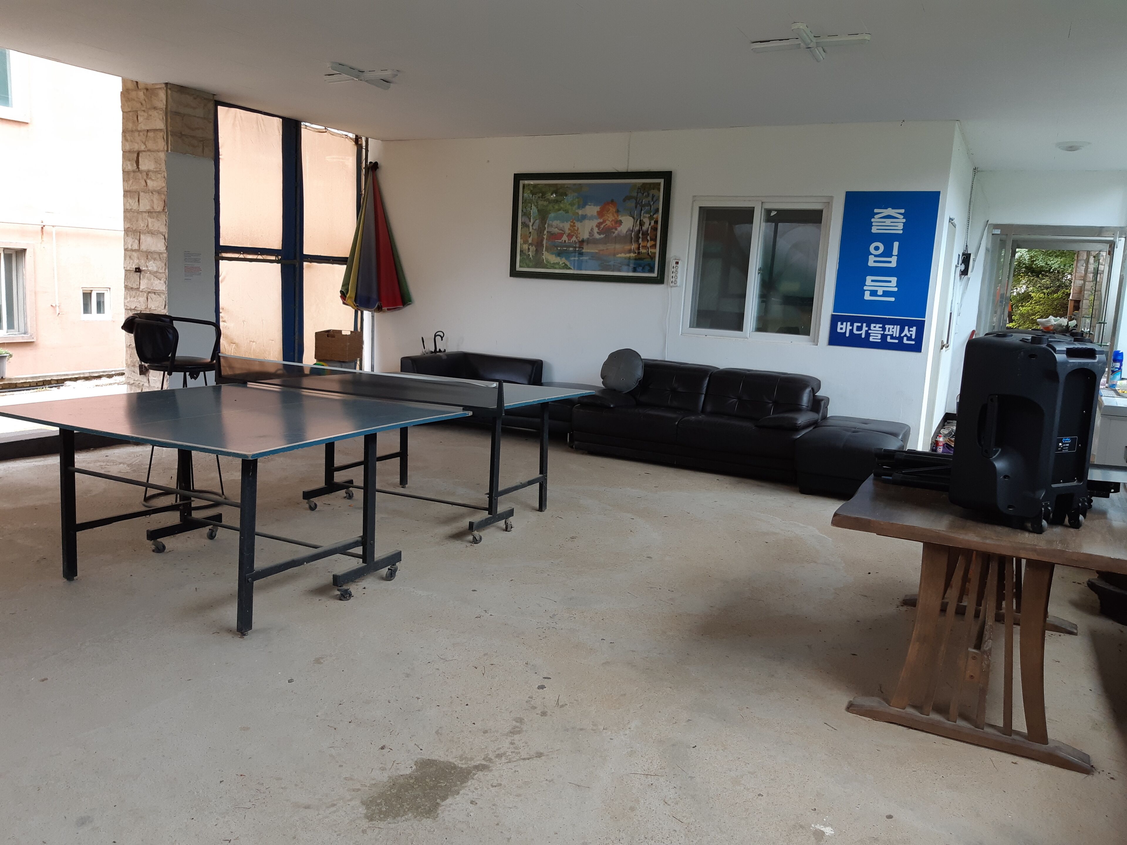 A room with a ping pong table, a black leather couch, a black suitcase, and a blue sign on the wall.