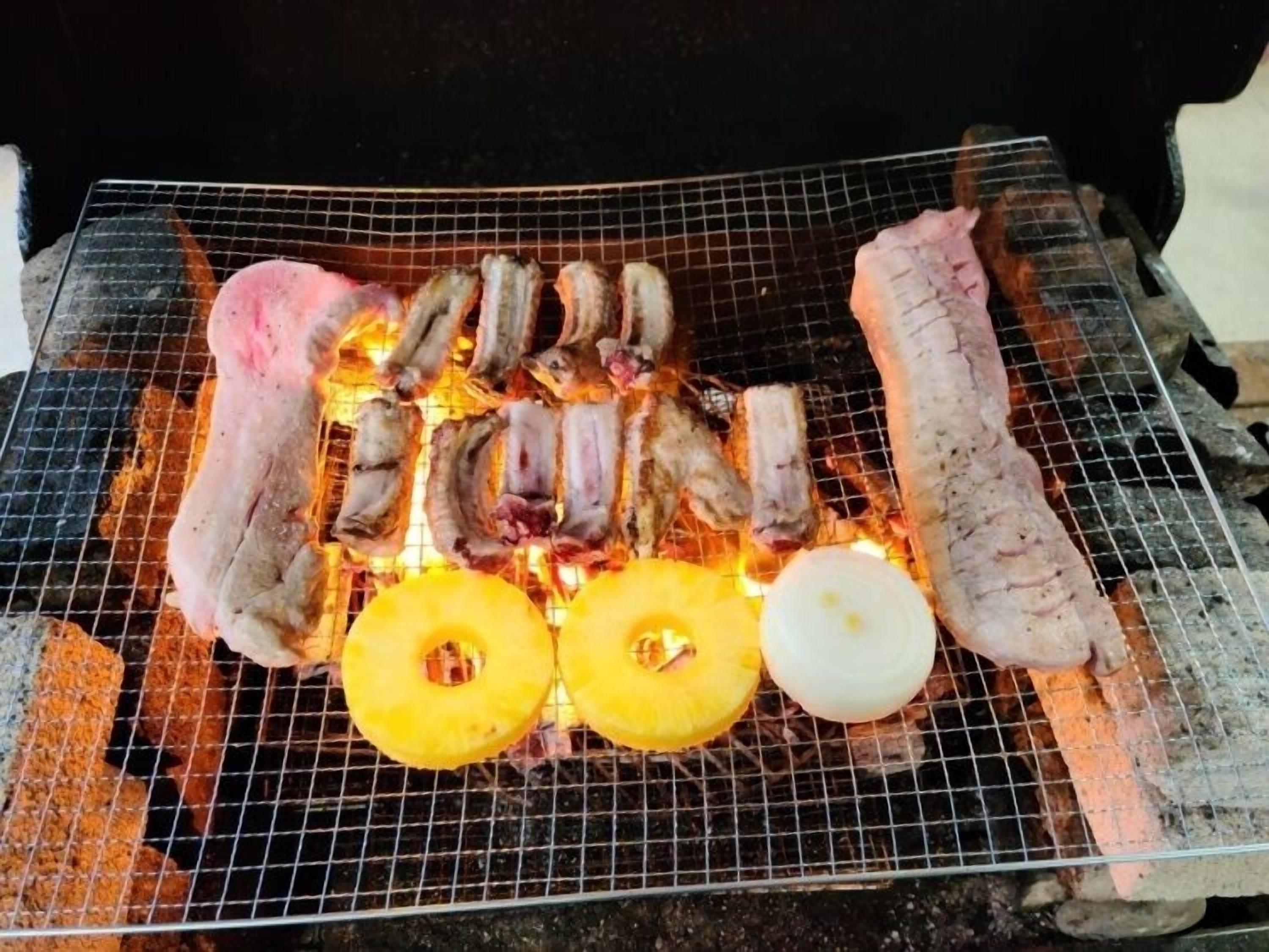Ein Grill mit verschiedenen Fleischsorten und Ananasstückchen.