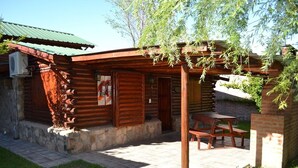 Ein rustikales Holzhaus mit überdachter Veranda, Steinfundament und einem Holztisch sowie einer Bank.