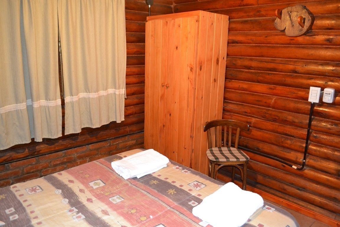 Una habitación de cabaña de madera con cama, una silla y un armario de madera.