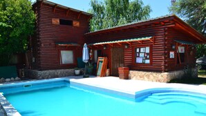 Eine Blockhütte mit Schwimmbad, Steinmauern und einer überdachten Terrasse.