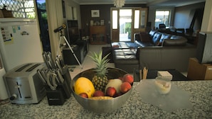A kitchen with a fruit bowl, toaster, and a dining area with a glass table. - Mount Gravatt Guesthouse (Mount Gravatt East)